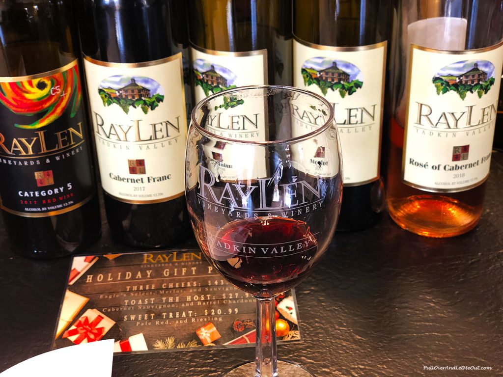 A glass of wine in front of several RayLen Wine bottles. PullOverAndLetMeOut