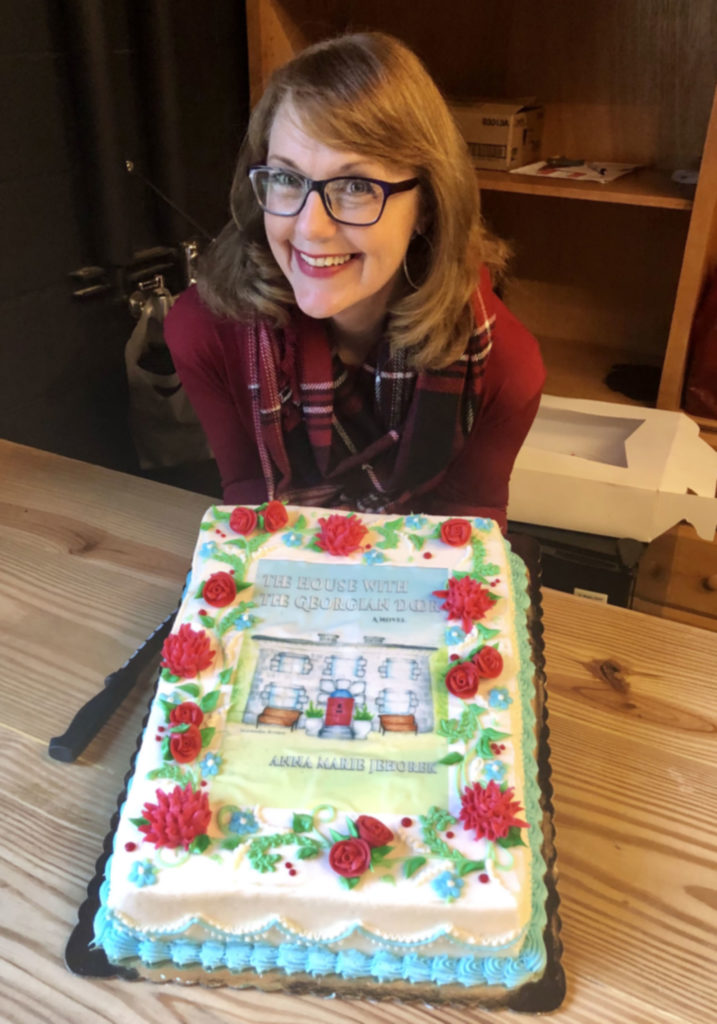 Author Anna Marie Jehorek with a cake decorated with the book cover of The House with the Georgian Door