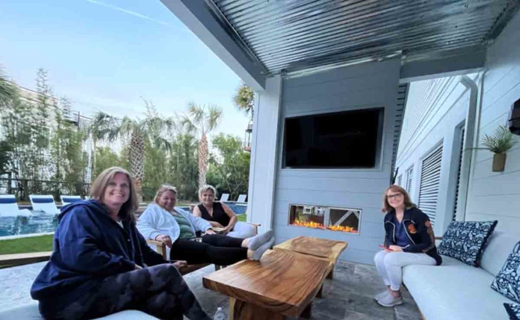 a group of women sitting by an outdoor fireplace.