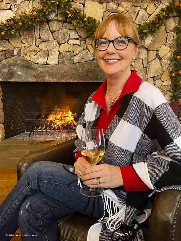 a woman with a glass of wine sitting by a stone fireplace.