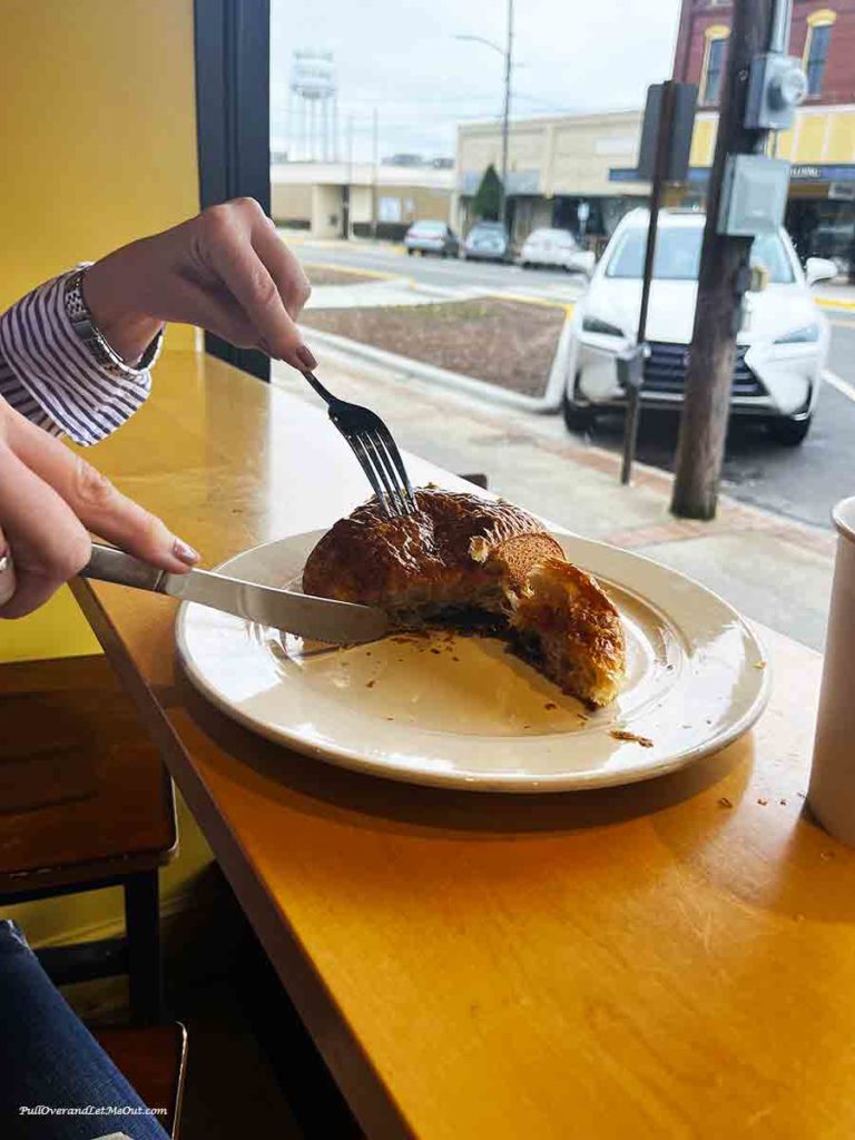 a woman with a fork and knife cutting into a chocolate croissant.