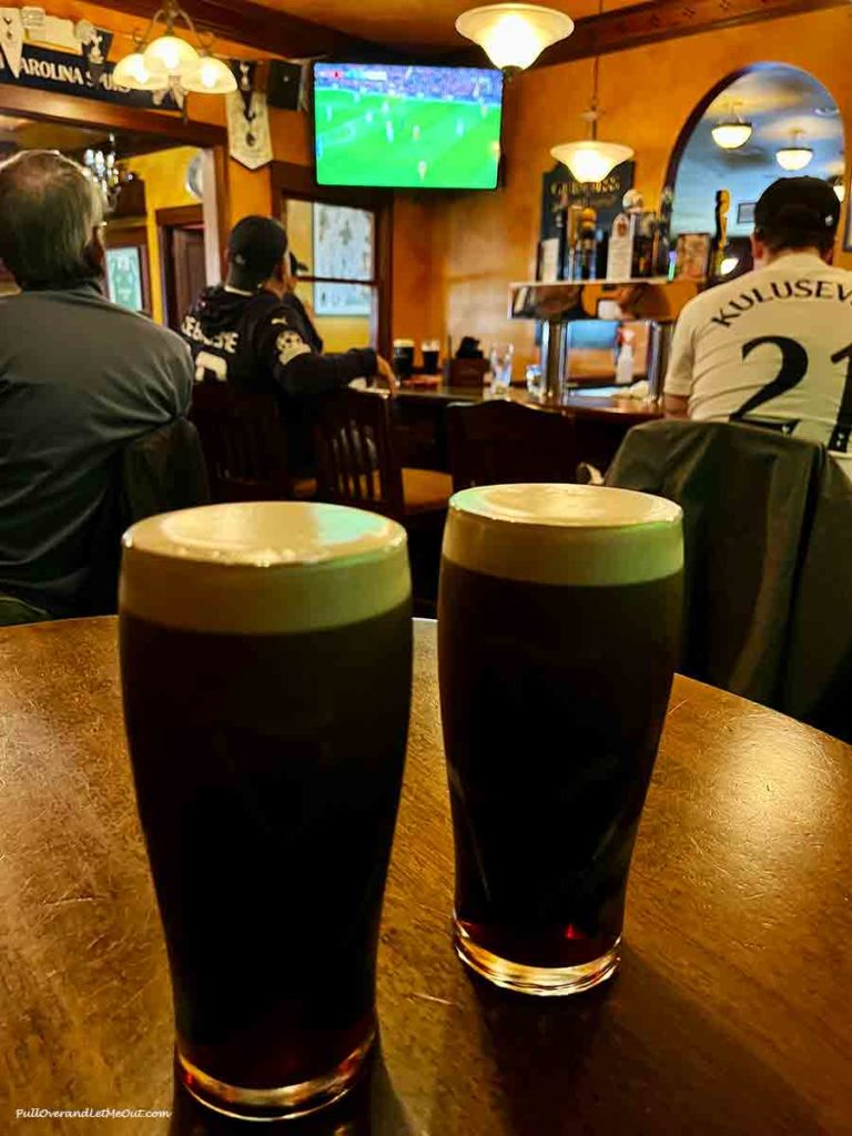 two pints of Guinness in a bar where people are watching soccer on tv