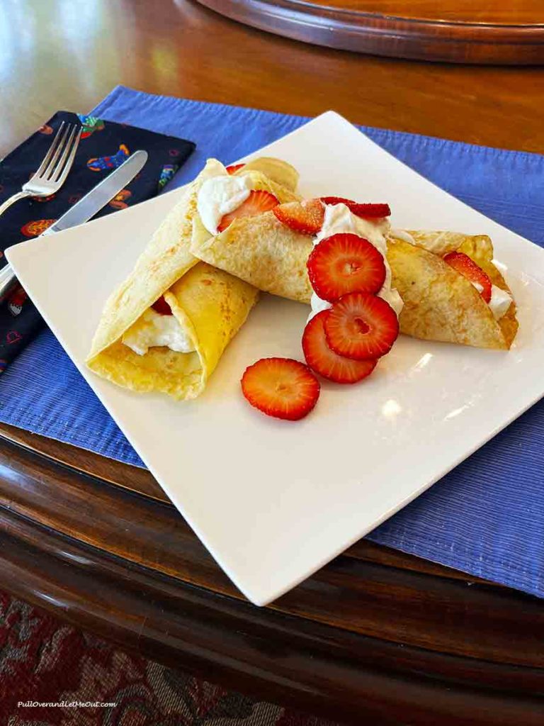a strawberry crepe on a white plate with a blue placemant
