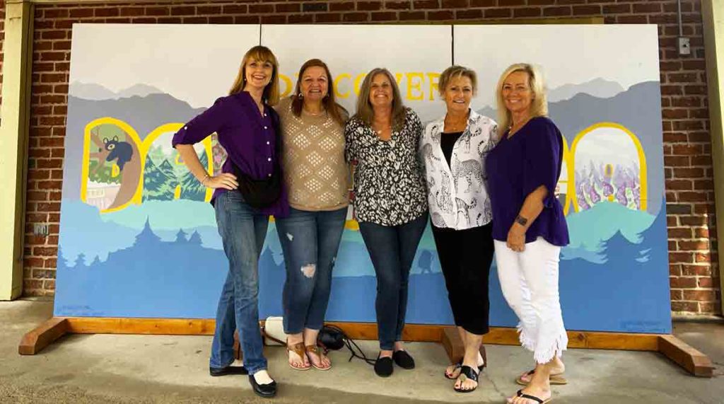 five ladies posing in front of a sign