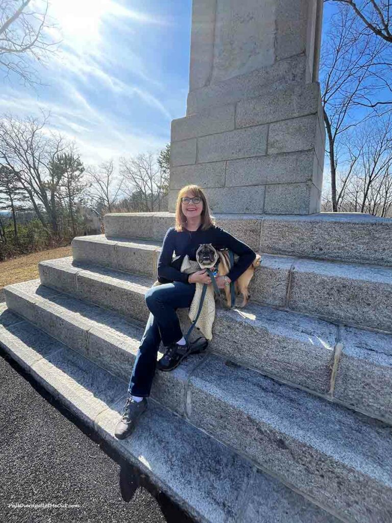 a woman and her pug sitting on the steps of a monument at Kings Mountain National Military Park