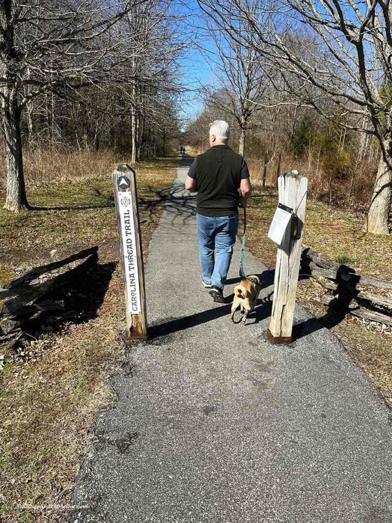 a man walking a small dog on a wooded trail