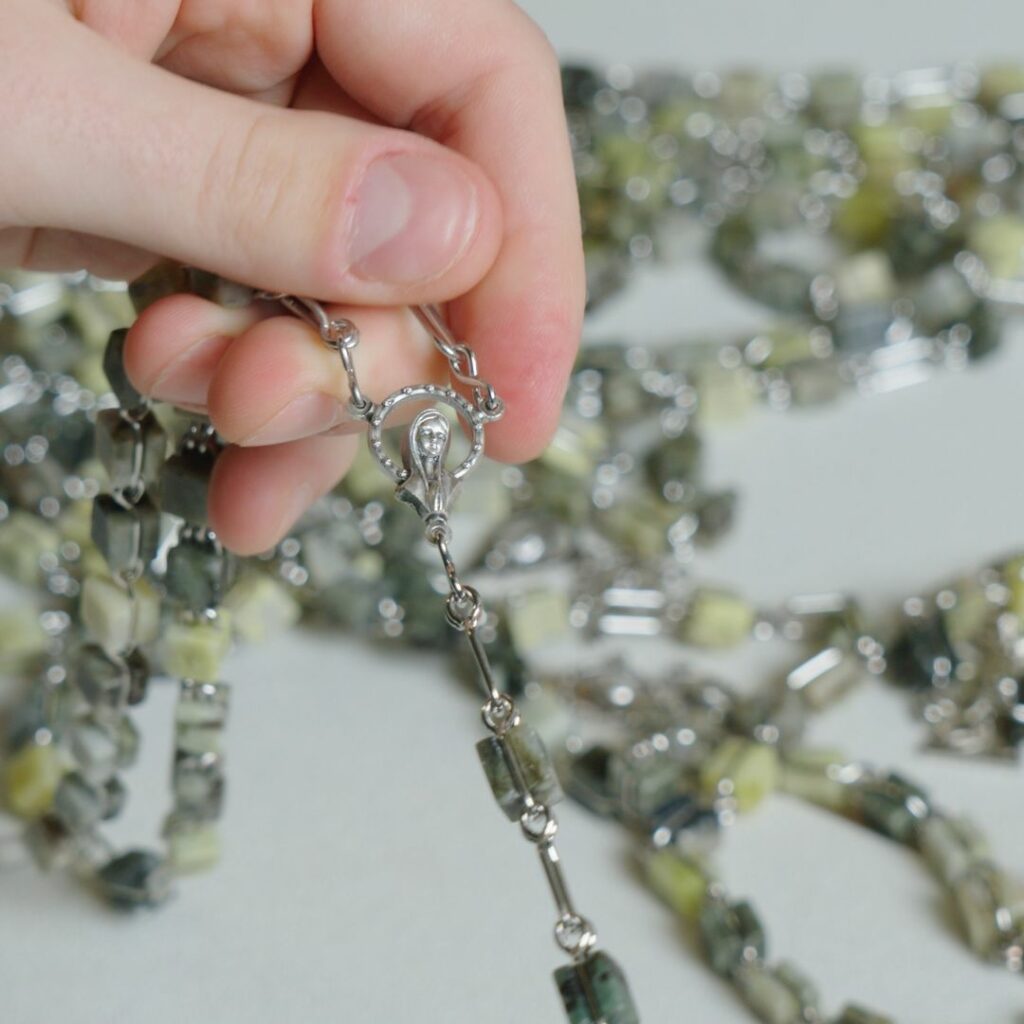 a hand holding a set of rosary beads made of Connemara Marble